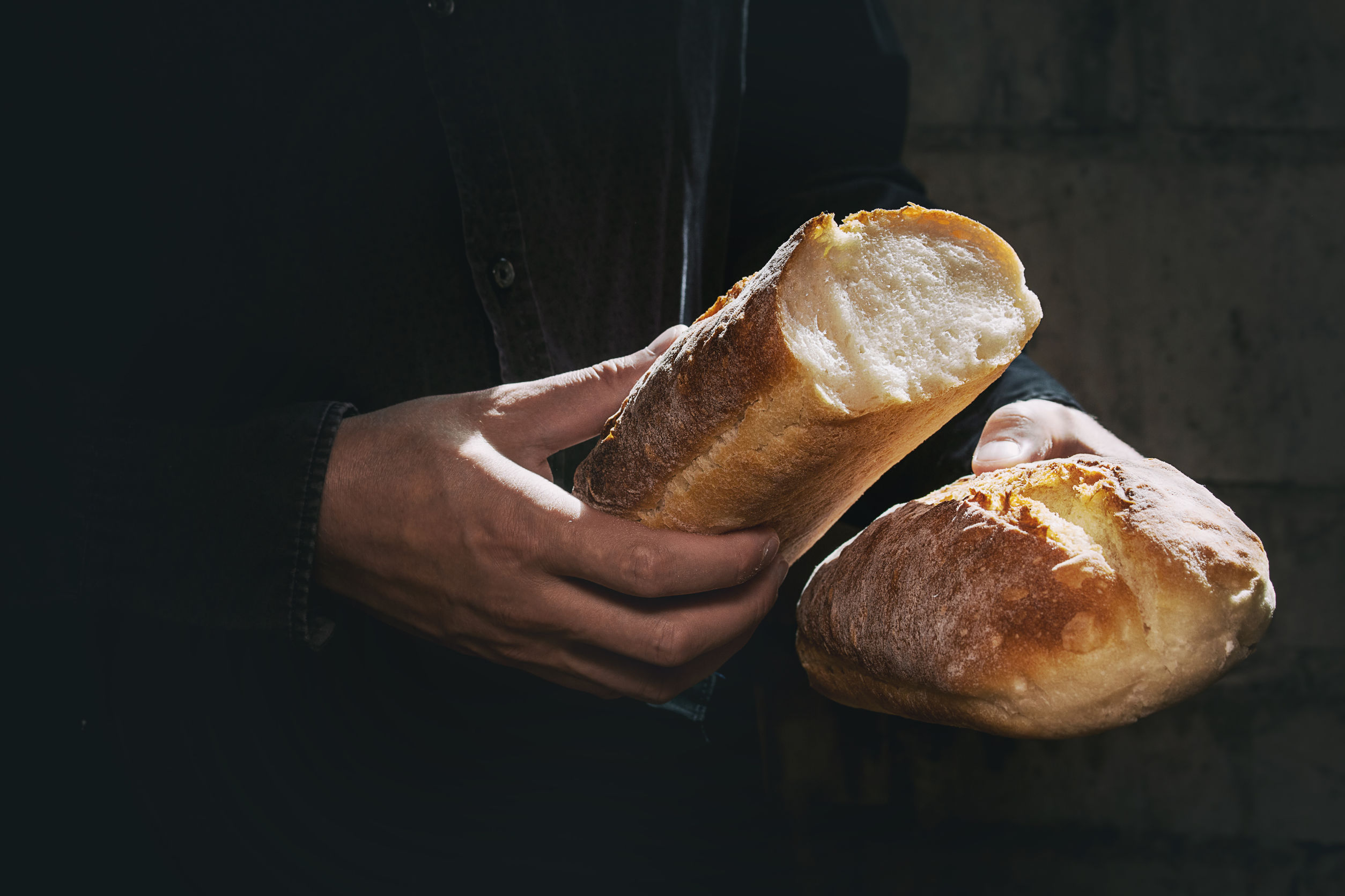 特寫，聚焦在一雙手。手拿著麵包，把它搣成兩半。